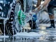 A person is washing a car tire with a green brush. Tire is covered in water and soap. Blue car wash with white soap foam. Auto care service. Car cleaning service concept. Vehicle cleaning service. 