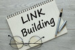 LINK BUILDING, Workplace with a notepad and glasses with a pen on a wooden table. text on the page