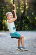 Portrait of a smiling boy riding on tight rope swing in sunny green bokeh background.
