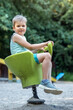 Happy child in outdoor playground, posing on spring swing.
