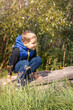 Portrait of a playful boy playing in sunny nature. A child crouch on a small concrete fence, vertical photo