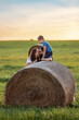 A happy family near a round roll of straw in a green meadow. The son is crouch high and watching his parents kiss