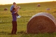A father carrying his little son on a meadow with straw rolls in the evening