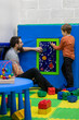 Father with his son in the sensory play room. The child performs logical and sensory tasks at the planet stand with the help of the parent