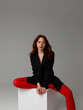 Beauty model woman . Model test portrait with young beautiful fashion model posing on grey background. Red Hair woman in a black blazer and red tights. Natural makeup