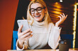 Cheerful hipster girl excited with good news reading  mail on smartphone sitting in coffee shop, emotional woman happy about getting discount for internet communication checking news on telephone