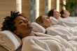 © Doni_Art - A group of people are relaxing in a spa room, wearing bathrobes with their eyes closed and lying on comfortable chairs in a hotel wellness or spa center.