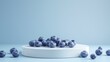 Fresh blueberries on a white pedestal against a blue backdrop.