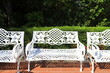 Summer garden furniture. Retro forged white benches in street cafe on terrace. Outdoor furniture, openwork bench in garden.