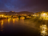 Fototapeta Uliczki - Misty River Nightscape: The Glow of the Old Bridge