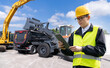 Engineer with a digital tablet on the background of construction machine.s