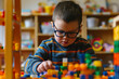 Little boy with glasses playing with colorful building blocks. Kid sitting in room alone and playing