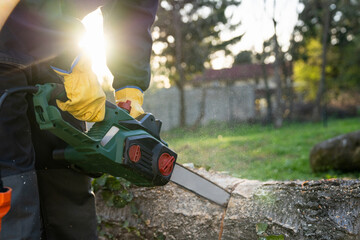 A man in uniform cuts an old tree in the yard with an electric saw.