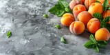 Fototapeta  - Fresh apricots and mint leaves spread on a textured gray surface.