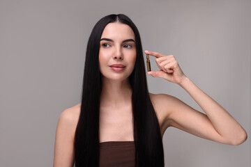 Canvas Print - Beautiful young woman holding skincare ampoule on grey background