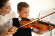 © New Africa - Young woman teaching little boy to play violin indoors
