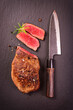 Barbecue dry aged angus roast beef steak with herbs and spice served as top view on a design board with a Japanese santoku knife