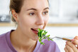 Young beautiful smiling woman eating fresh organic vegetarian salad sitting in the kitchen at home