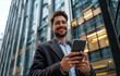 © Impressionstock - A young businessman engaging with his smartphone against a backdrop of sleek urban architecture.