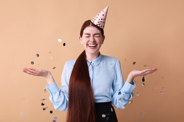 Wall Mural - Happy woman in party hat and falling confetti on beige background