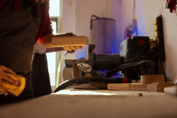 Sticker - Man in assembly shop using sandpaper for sanding wooden surface before painting it, ensuring adequate finish. Carpenter using abrasive sponge to fix surface damages suffered by wood