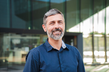 Bearded mature man smiling and looking at camera. Middle aged male entrepreneur staring front with friendly and confident expression. Individual portrait of a mid adult guy wearing blue shirt