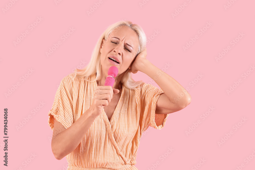 Mature woman with vibrator singing on pink background