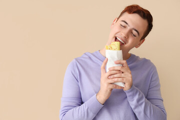 Wall Mural - Young man eating tasty sandwich wrap on beige background