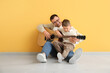 © Pixel-Shot - Happy father and his little son playing guitar near yellow wall
