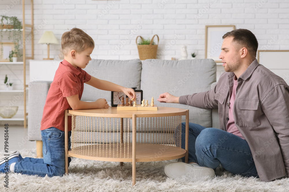 Father and his little son playing chess at home