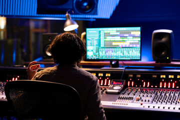 Fototapete - Audio expert working on editing music with daw software interface, processing and mixing sounds in control room. Skilled engineer operating on control panel board console, mixer station.