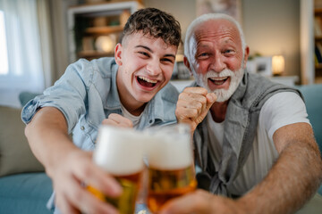 Wall Mural - teenager and his grandfather senior man watch football game at home