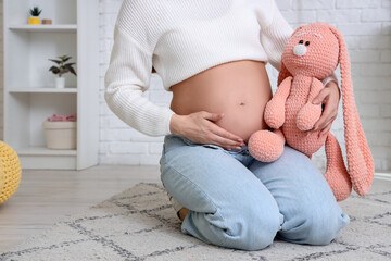 Sticker - Young pregnant woman with toy bunny sitting on floor in children's bedroom, closeup