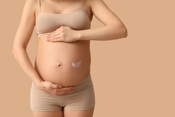 Wall Mural - Young pregnant woman with cream against stretch marks on beige background