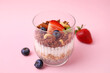 Tasty granola with berries, nuts, yogurt and chia seeds in glass on pink background, closeup