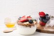Tasty granola with berries, yogurt and almond flakes in plastic cup on white table, closeup
