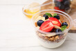 Tasty granola with berries, yogurt and almond flakes in plastic cup on white wooden table, closeup. Space for text
