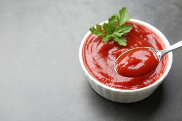 Wall Mural - Taking delicious tomato ketchup with spoon from bowl at grey textured table, closeup. Space for text