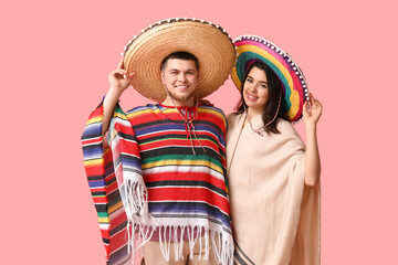 Canvas Print - Beautiful young happy couple in sombrero hats and poncho on pink background. Cinco de Mayo celebration