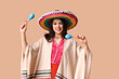 Beautiful young happy woman in sombrero with maracas on beige background. Cinco de Mayo celebration