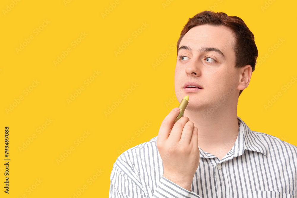Handsome young man applying lip balm on yellow background