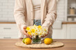 Young woman with bouquet of daffodils and fruits on table at home