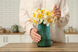 Young woman touching vase with yellow flowers on table in stylish kitchen