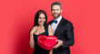 Couple in love isolated on red. Birthday couple with gift. Loving man giving present gift box for Valentines day to surprised woman. Man receiving present. Happy Valentines day. 14 February