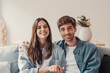 Portrait of young 20s just married couple in love posing photo shooting seated on couch in modern studio apartments, concept of capture happy moment, harmonic relationships, care and sincere feelings.