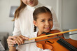 © New Africa - Young woman teaching little girl to play violin indoors