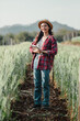 © Satori Studio - Happy female farmer with a notebook stands amidst tall wheat, wearing a straw hat and red plaid shirt in the field.