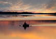 Man fishing on lake from small rowing boat at sunset or sunrise time. Fisherman silhouette at sunset