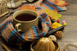 Autumn mood in the form of a cup of tea and a warm scarf. Maple leaves are scattered on a wooden table. Home comfort and warmth of hot tea.