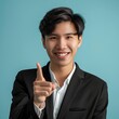 The photo shows a young man of Asian descent, with short dark hair and wearing glasses. He is wearing a dark suit jacket and shirt, and has a friendly smile on his face. He is pointing his finger at t
